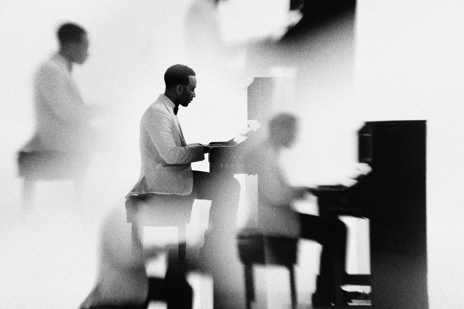 John Legend at an upright piano in a white studio, the exposure doubled so he appears twice